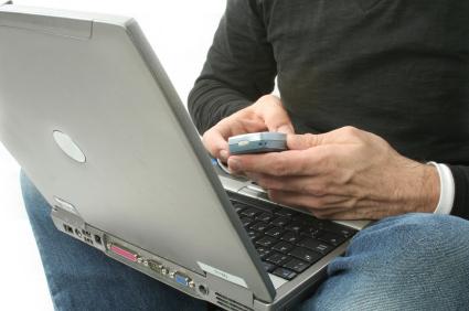 Hands holding cellphone and using computer