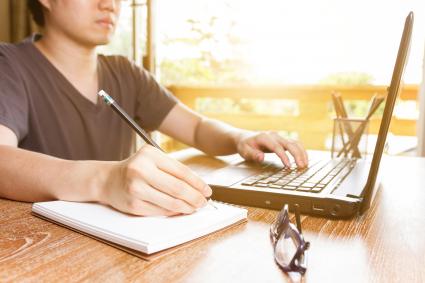Man using laptop and writing on tablet