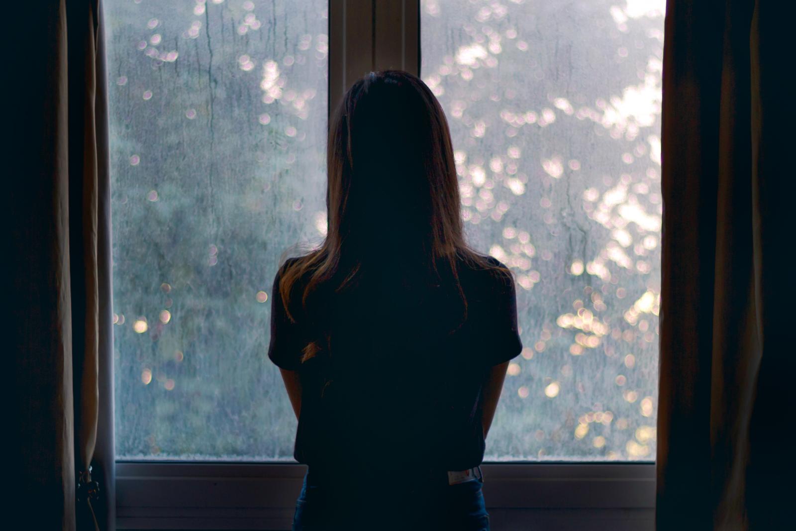 Silhouette of depressed woman looking through a window