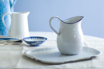 Enameled white pitcher in foreground on enamel platter, with porcelain and enameled pitchers in background. 