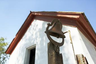 Farm bell sits in front of a historic farm house