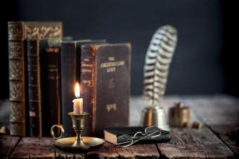 Study area with old books, quill pen and antique candle holder on an old wood desk