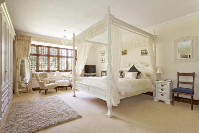 White four-poster bed in large neutral-colored bedroom