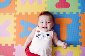 Cute baby girl relaxing on colorful alphabetical puzzle playmat