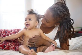 Mother holding smiling baby daughter on bed