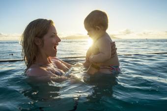 Woman playing with her little baby in the ocean at sunset 