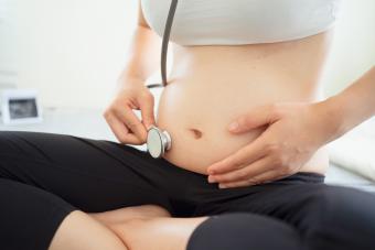 pregnant woman using stethoscope checking heartbeat of baby