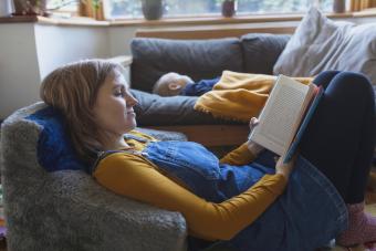 Woman reading book in living room with little son sleeping