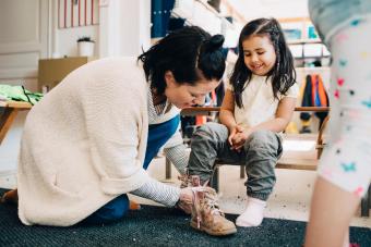 teacher helping happy girl wearing shoes