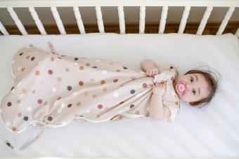 Baby in sleeping bag laying down in a crib