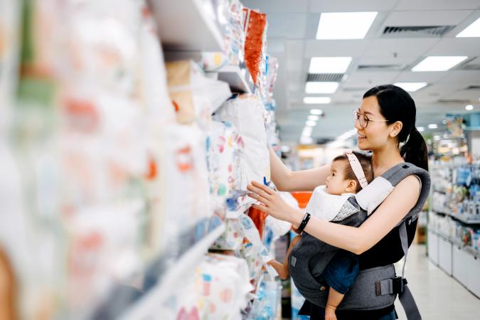 Young mother carrying cute baby girl shopping for diapers