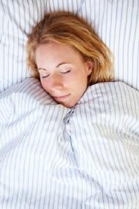 Woman snuggling under comforter.