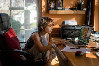 A preteen boy sits at computer playing an online chess game