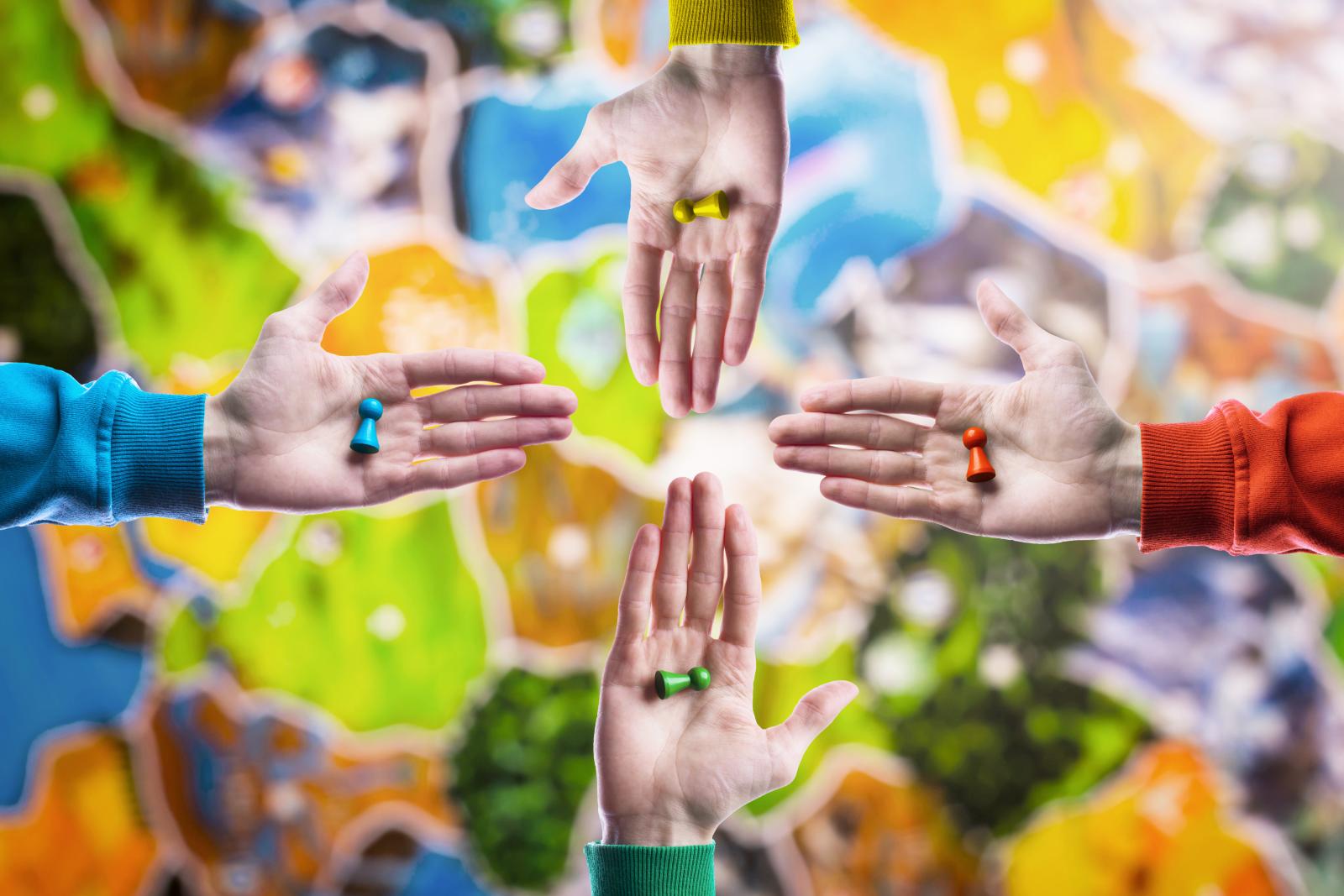 People holding in hand colourful playing figures on blurred board game field background