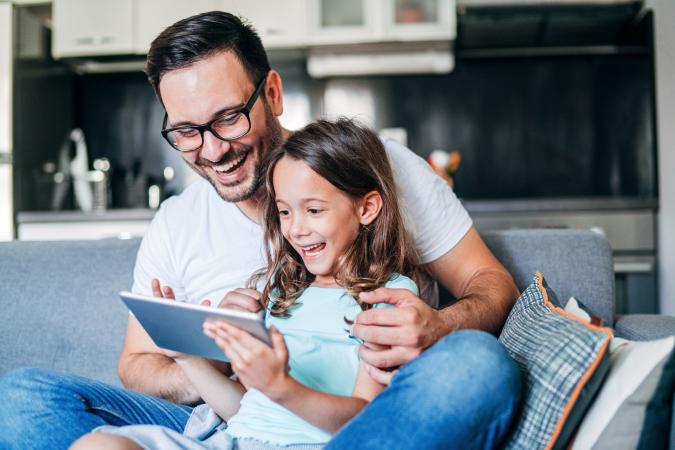 Young father and his cute small daughter having fun with digital tablet on couch