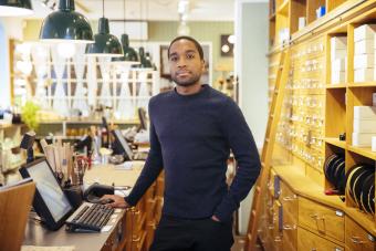 Confident young male entrepreneur standing behind store counter