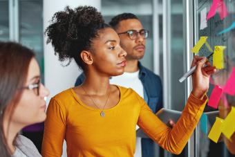 Businesswoman standing with her colleagues writing new ideas on sticky notes