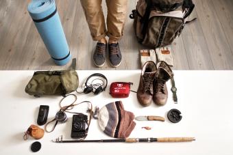Low section of man standing with hiking and fishing gear arranged on table at home