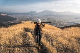 A photographer carrying her tripod hiking up a mountain