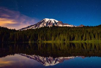 Snowcapped Mountain And Pine Trees Against Sky Reflecting In Lake During Sunrise At Mt Rainier National Park