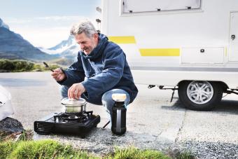 man cooking on turist stove nearby campervan in mounatins