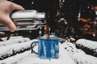 Cropped Hand Pouring Tea In Cup On Snow Covered Log