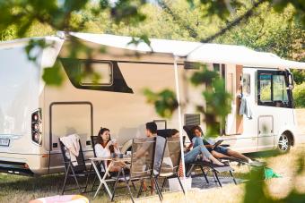 Family relaxing on chairs outside camper van at campsite during summer vacation