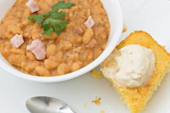 Bowl of navy bean soup garnished with fresh green parsley and pieces of ham