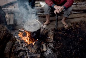 Man sitting on log, watching cooking pot on campfire