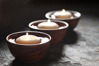 Three lit candles floating in wooden bowls filled with water