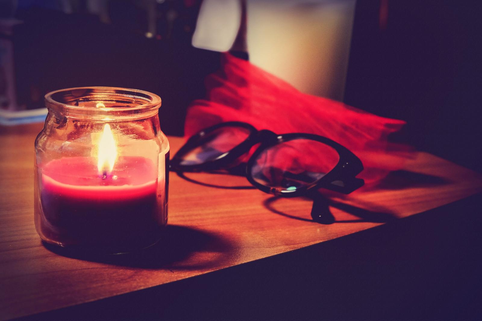 Lit Candle In Jar And Eyeglasses On Table