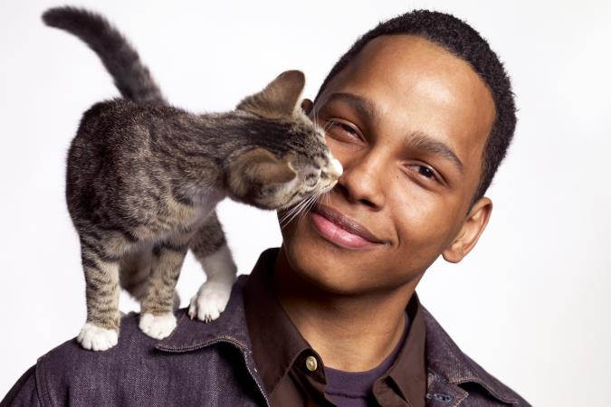 CatYoung man with cat on shoulder that it's licking his face