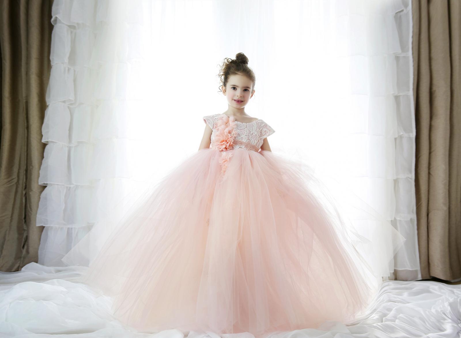 Beautiful little girl wearing a princess gown and standing in front of large window