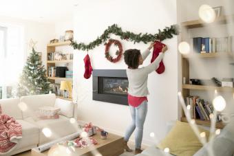 Woman hanging Christmas stockings above fireplace in living room