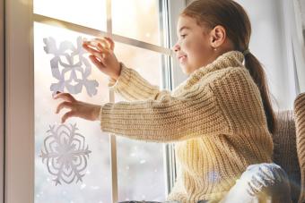 girl hanging paper snowflakes in window