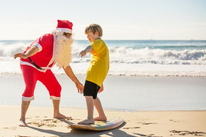 Australian summer Santa Claus showing young boy how to surf