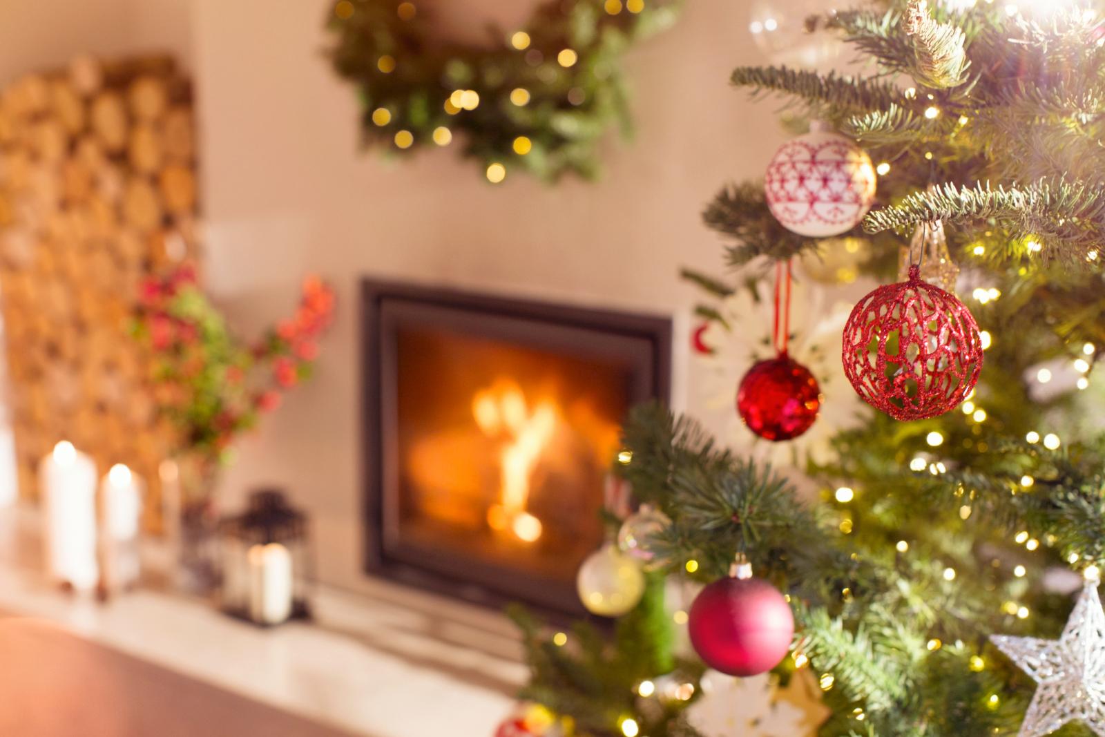Red and white ornaments hanging from Christmas tree next to fireplace