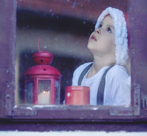 Child looking out snowy window at Christmastime.