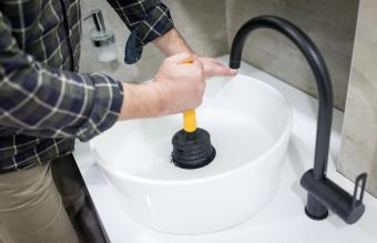 Plumber's hand using plunger in bathroom sink