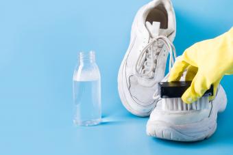 woman wearing rubber gloves cleaning salt stains from white sneakers with a brush.