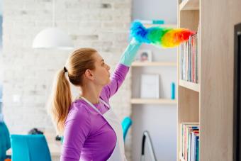 Young woman in white apron dusting books