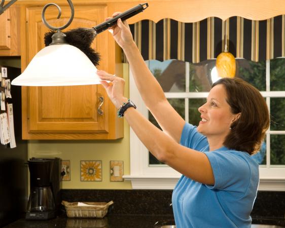 woman using duster to dust kitchen lamp ahdes