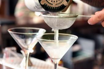 Bartender pouring martinis into chilled glasses 