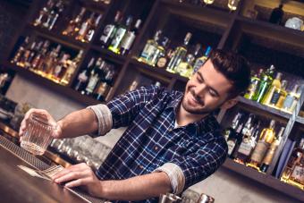 Young bartender standing at bar counter holding glass and taking money for tip