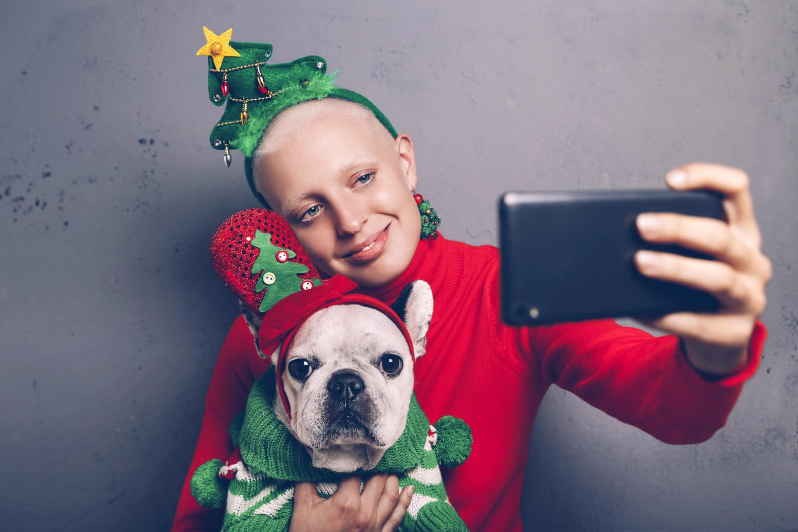 Woman with French bulldog taking selfie with smartphone at Christmas time