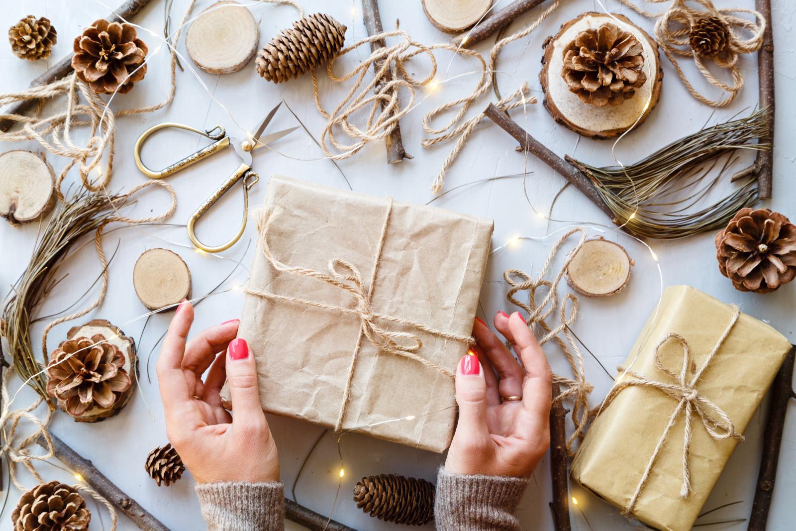 Cropped Hands Holding Gift By Christmas Decorations On Table