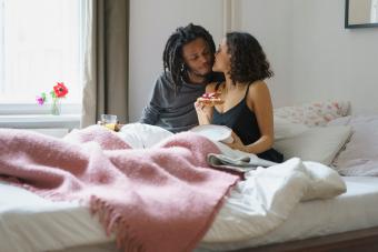 Young woman kissing man while holding pie in bed at home 