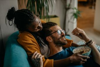 Couple cuddling on couch, eating popcorn and watching TV