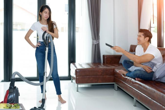 Woman vacuuming and husband watching media