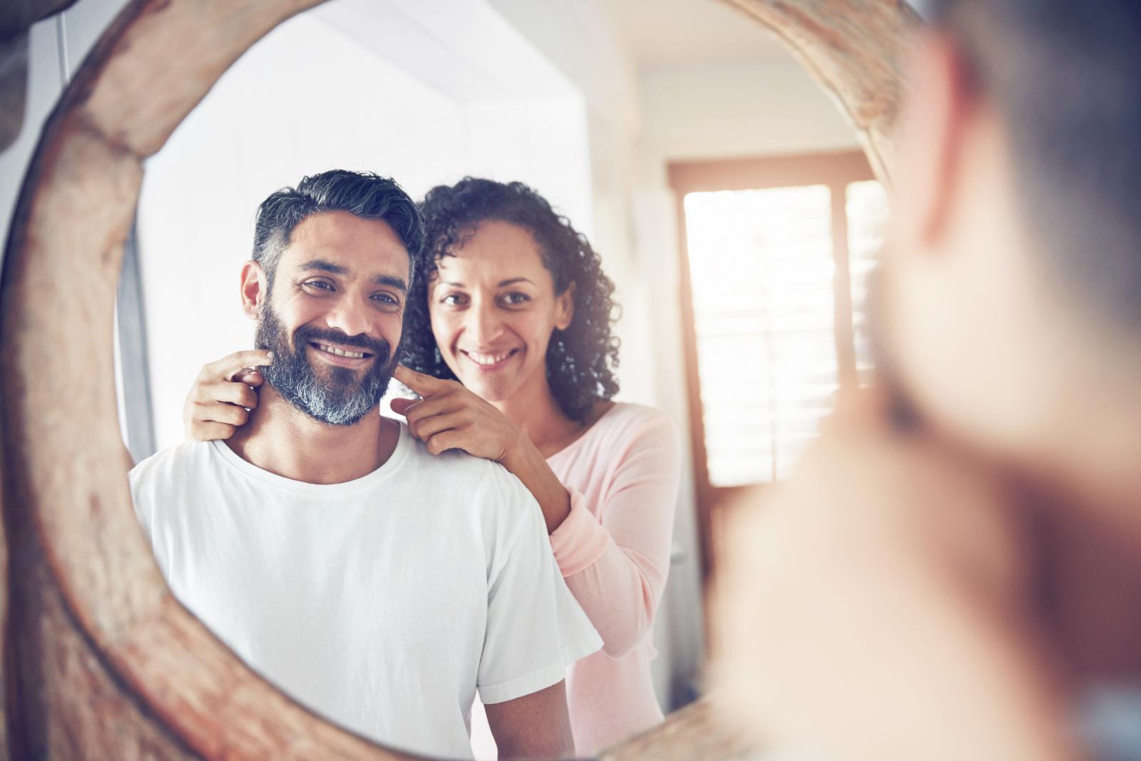Shot of a mature man looking at his reflection in the mirror with his wife encouraging him to smile